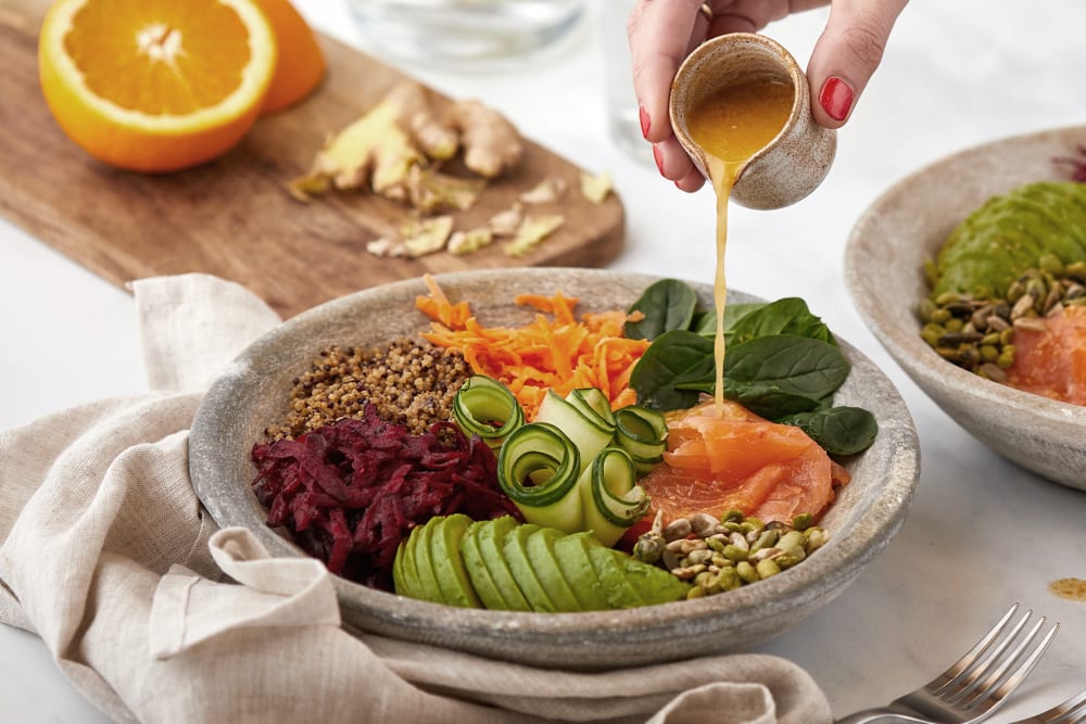 Person pouring a dressing onto a healthy mixed salad